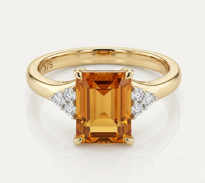 A yellow gold ring featuring a large rectangular emerald-cut orange citrine center stone, accented by small round-cut diamonds on either side of the band. The inside of the band is stamped with '375'.